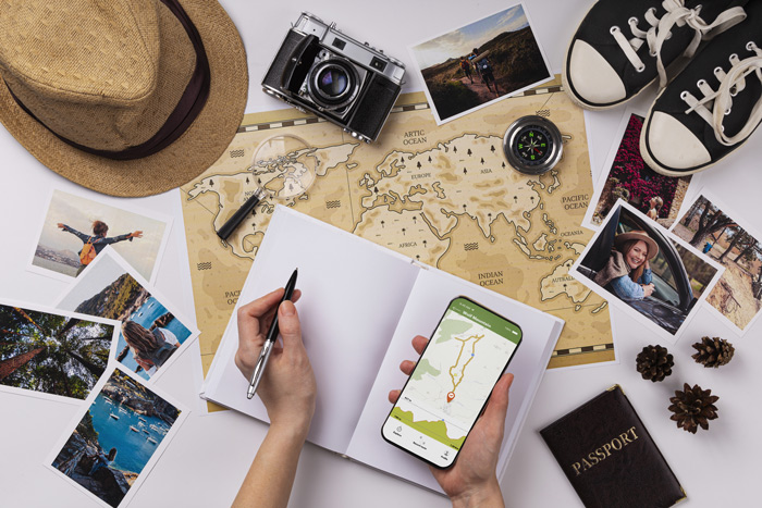 Mapa-múndi com câmera, chapéu, fotos, passaporte, celular com rota de trilha e acessórios de viagem organizados, representando o planejamento de aventuras ao lado de um acompanhante para viagem.