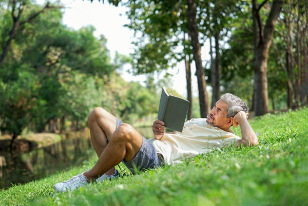 Homem lendo ao ar livre na grama, expondo-se à luz natural para evitar efeitos do jet lag.