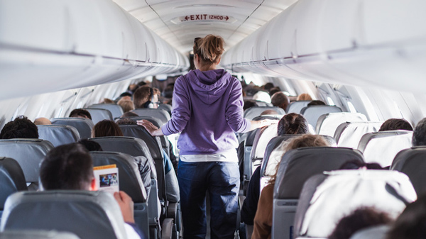 Cabine de avião com pessoas sentadas e em pé, fazendo caminhada para evitar jet lag.