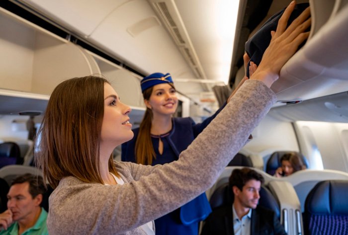Passageira guardando bolsa com medicamentos no compartimento de malas do avião.