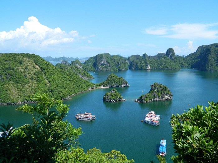 Mirante da Baía de Ha Long com ilhotas verdes e embarcações cruzando o mar azul em dia claro.