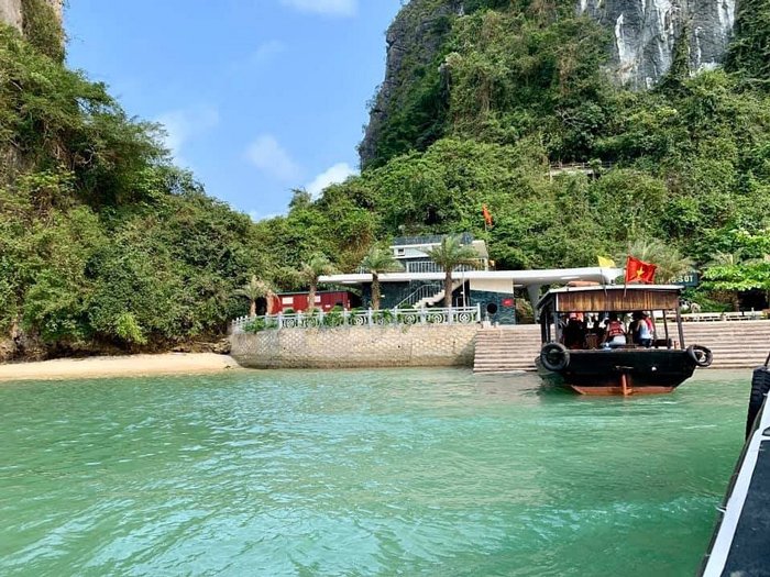 Píer cercado por falésias na Baía de Ha Long, barco tradicional aguardando embarque para passeio entre as ilhas.