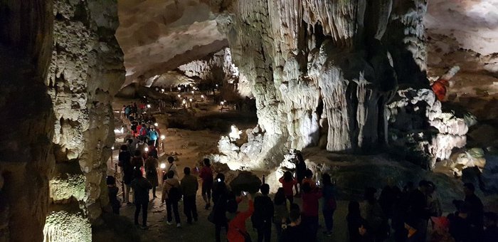 Interior da caverna Súng Sốt na Baía de Ha Long, com estalactites iluminadas e visitantes em passarelas.