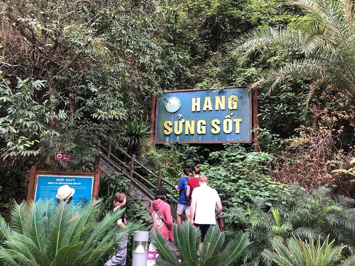 Entrada da Hang Sửng Sốt na Baía de Ha Long, placa indicando a trilha em meio à vegetação tropical.