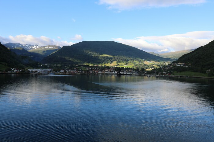 Vista aérea do Sognefjord, mostrando o fiorde profundo entre montanhas íngremes, com um barco cruzando as águas e criando rastros suaves. 