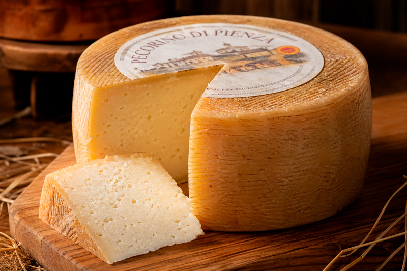 Imagem de um queijo pecorino com rótulo, com uma fatia cortada.