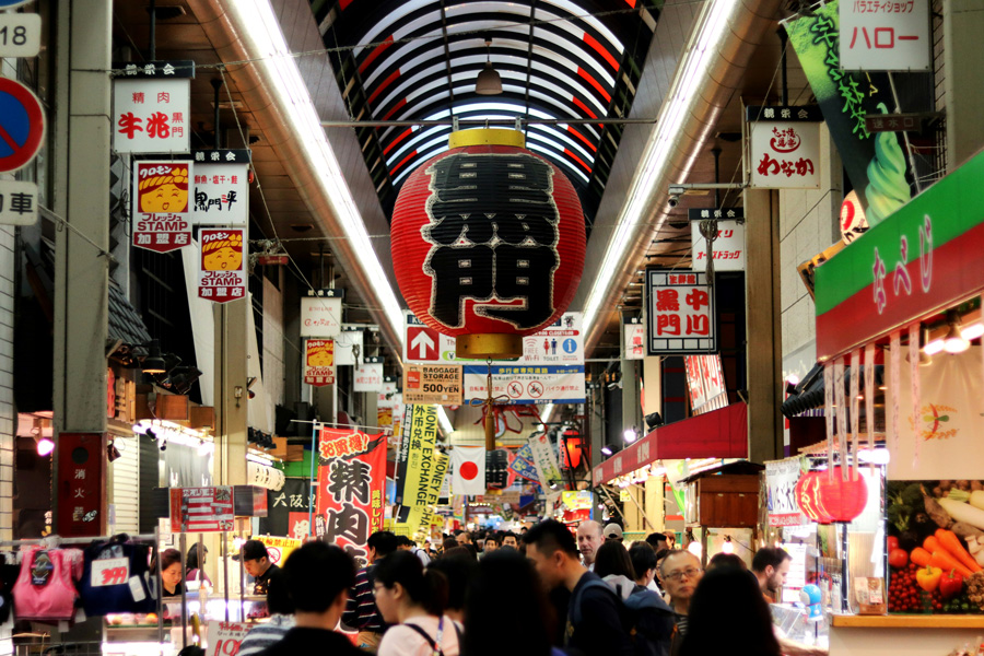 Interior do Mercado Kuromon em Osaka, com barracas de alimentos e visitantes