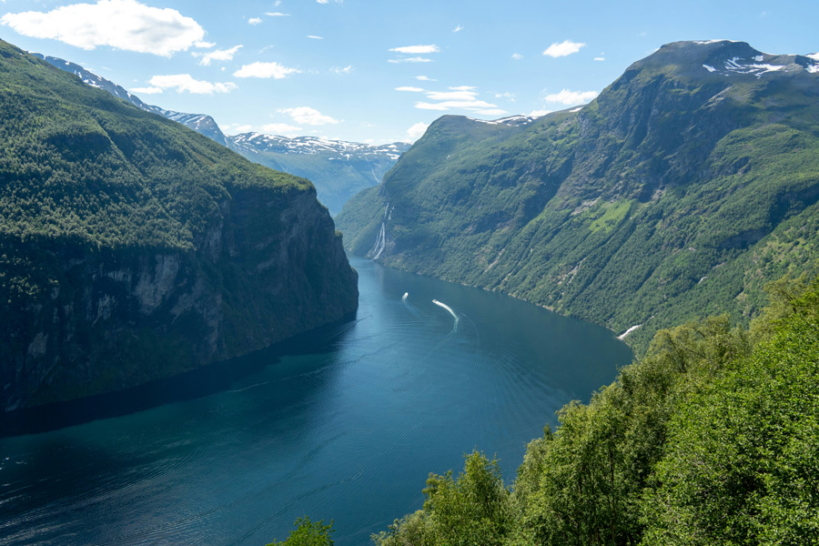 Fiorde norueguês cercado por montanhas verdes e íngremes, com águas tranquilas entre os vales.