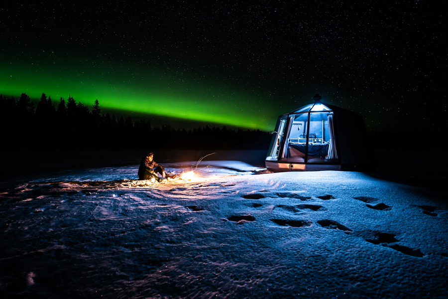 Aurora boreal iluminando o céu noturno sobre uma paisagem coberta de neve na Lapônia.