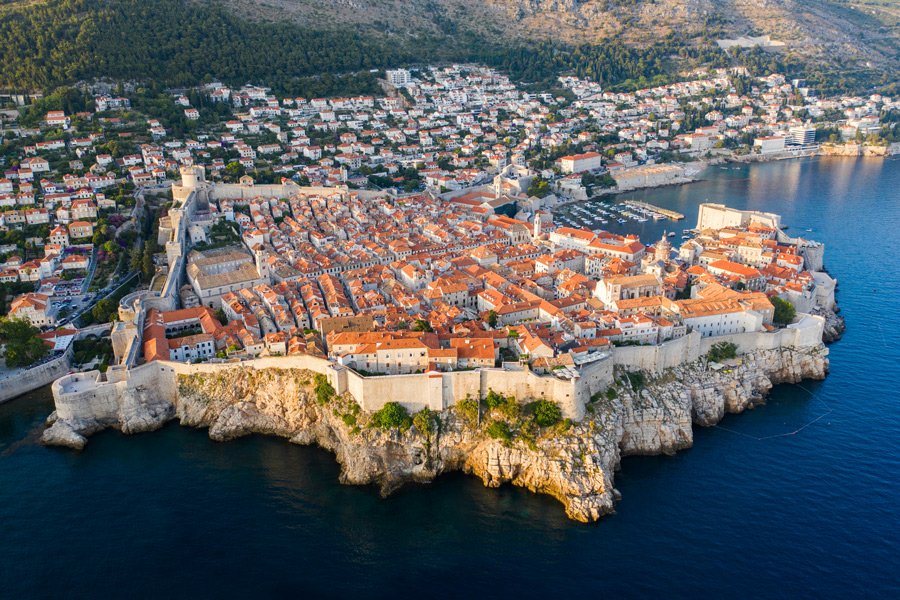 Vista aérea da cidade histórica de Dubrovnik, na Croácia, com suas muralhas de pedra e o Mar Adriático ao fundo.