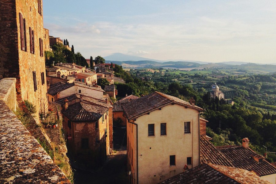 Paisagem rural da Toscana, na Itália, com construções de pedra, colinas verdes e vegetação mediterrânea.