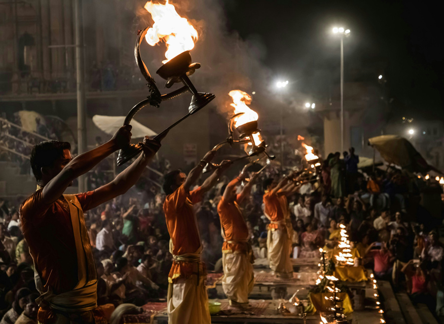 Sacerdotes erguem lamparinas acesas durante a cerimônia Ganga Aarti, à noite, diante de uma multidão nos ghats de Varanasi, na Índia.
