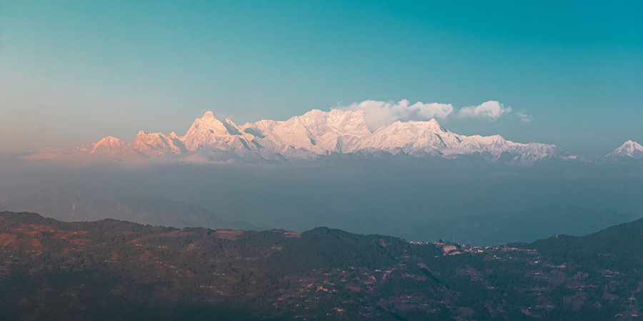 Picos nevados da cordilheira do Himalaia iluminados por uma luz rosada, acima das colinas do vale de Katmandu, no Nepal.