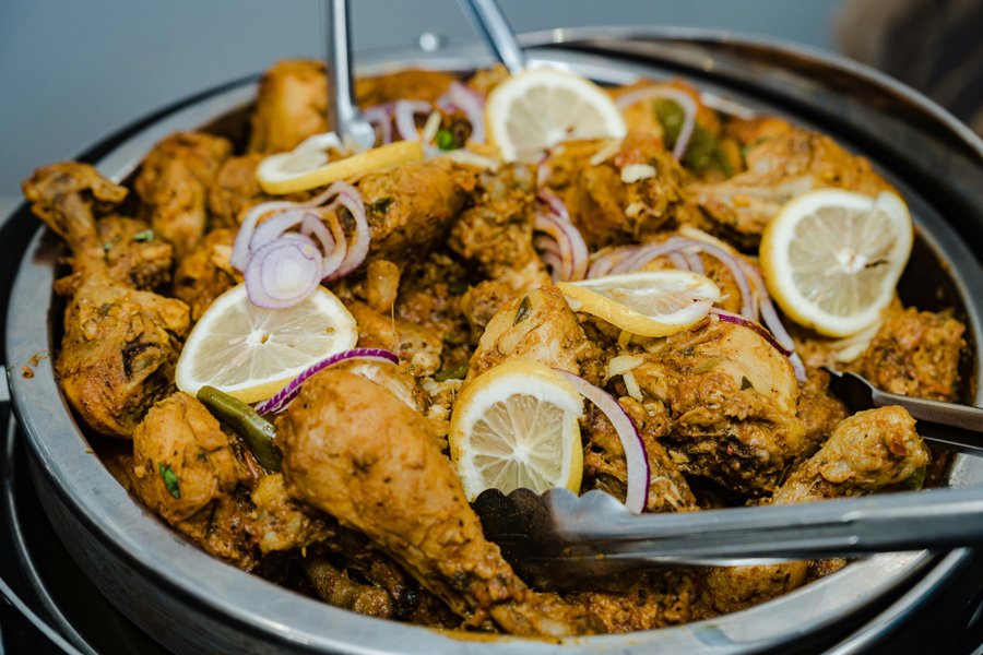 Frango tandoori com cebola roxa e rodelas de limão servido em uma panela, prato típico da culinária do norte da Índia.